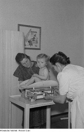 Krankenschwester wiegt ein Kleinkind im Beisein der Mutter