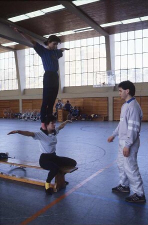 Frankfurt (Main), Otto-Fleck-Schneise 4. Deutsche Sportschule, Sporthalle. Bei einem Kurs für Zweierkunstfahrer werden Schulterstandsübungen ohne Rad trainiert