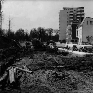 Mewesstraße: Stützmauer beim Kreishaus: Blick Richtung Kurparkallee: vorn Baustelle mit Baumaterial und Bagger: rechts Pkws: hinten links Kurpark mit Bäumen: hinten rechts hinten Wohnhäuser und Hochhaus "Liebe"