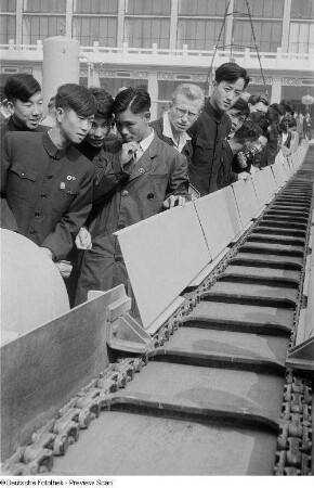 Besucher der Leipziger Herbstmesse 1954 wohnen der Vorführung eines Förderbandes der chinesischen Sektion bei