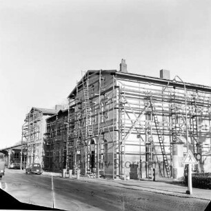 Bahnhofsgebäude: Streichen der Fassade: mit Gerüst und Leitern: rechts Litfaßsäule, Straßenlampe, Verkehrsschild: vorne Bahnhofstraße, Mülltonnen, links parkender Pkw