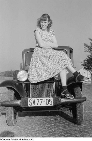 Porträts Renate Rössings auf der Kühlerhaube eines Opel 1,2 sitzend