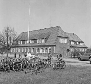 Volksschule: Hamburger Straße: Altbau: vorn links Ständer mit Fahrrädern: dahinter Schüler: rechts Pkw