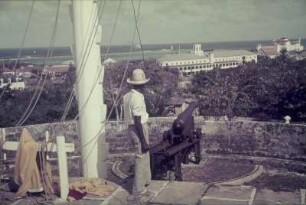 Reisefotos. Blick von einer Festungsplattform mit Kanone zu einem vor der Küste ankernden Passagierschiff