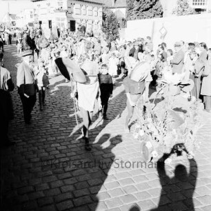 Karpfenfest: Umzug: Bahnhofstraße: mehrere Fußgruppen, mit umgestaltetem Kinderwagen: an den Straßenrändern Zuschauer: im Vordergrund Schatten des Fotografen: im Hintergrund Bildmitte Einmündung von Bischofsteicher Weg, 11. Oktober 1959