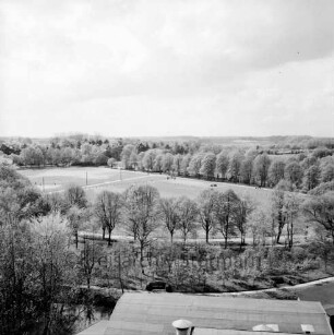 Vogelperspektive: von Silo der Weizenmühle ("Gloria-Mühle") der Johannes Ströh Mühlenwerke am Pferdemarkt: Blick nach Westen: Bürgerpark, Exer, Personen auf Spielfeld: hinten Gebäude der ehemaligen Flussbadeanstalt, Jugendheim, Uferbäume an Trave: vorne Uferweg, Mühlenarm der Trave: im Vordergrund Dach Betriebsgebäude von Ströh
