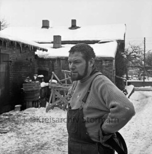 Bildhauer Rolf Goerler vor der alten Schmiede: Ausbau zum Atelier: hinten Holzböcke und Kisten: Winter