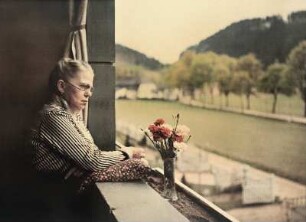Alte Frau auf einem Balkon mit einer Vase mit Nelken