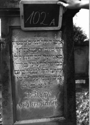 Grabstein 102 (Index: 99937109) Material: Sandstein Zustand: verwittert Maße HxBxT: 173x48x23 cm Beschreibung: konische Stele, Sockel, Giebel, rechteckiges Schriftfeld eingetieft Symbolik: Levitenkanne: Grabstein 102A