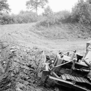 Feldmark: Anlage eines Anglerteichs: vorn rechts Bagger beim Zusammenschieben der Erde: an den Böschungen Büsche und Bäume