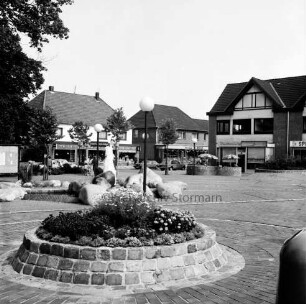 Rathausvorplatz [späterer Europaplatz]: Springbrunnen aus Findlingen: davor ummauertes Blumenbeet: im Hintergrund Poststraße mit Geschäften und Fußgängern
