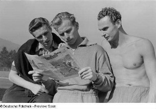 Porträt Hans Haberhauffes, Paul Tiedemanns und eines weiteren Mannes bei der Lektüre der Zeitung "Der Handball" auf dem Sportplatz der Sportschule