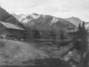 Dorf : Landschaft mit einer Holzhütte. Im Hintergrund bewaldete Berge