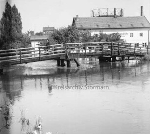 Trave: Hochwasser: vorn links Grünpflanzen: in der Mitte Kranbrücke: darauf Mann: hinten rechts Gebäude der Hamburger Tapetenfabrik: dahinter Gasometer der Stadtwerke: hinten links hinter Bäumen Häuser an der Lübecker Straße