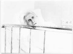 Alte Frau schaut über den Rand eines Krankenbettes (Altersgruppe 18-21)