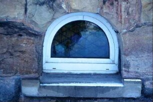 bogenförmiges Keller-Fenster im Bruchsteinsockel