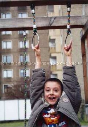 An Seilen hängender kleiner Junge auf einem Spielplatz (Altersgruppe 14-17)