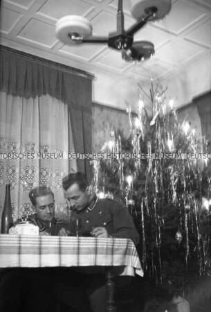 Zwei deutsche Soldaten an einem Tisch, im Hintergrund ein mit Lametta geschmückter Weihnachtsbaum