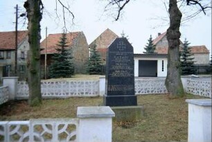 Kriegerdenkmal zwischen zwei Bäumen; Betonformsteinmauer