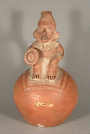 Applikation: sitzende anthropomorphe Figur mit Schild