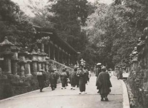 Nara, Japan. Shinto-Schrein Kasuga-Taisha. Touristen auf einem mit steineren Heiligen Laternen gesäumten Weg des Nara-Parks