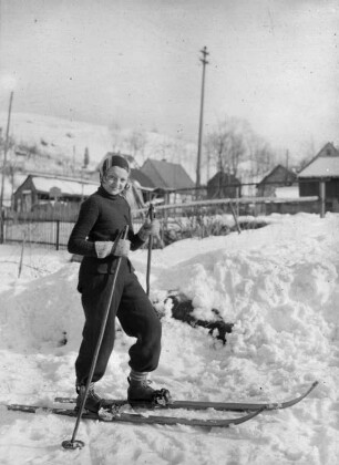 Mädchen mit Skiern vorm Haus des Fotografen