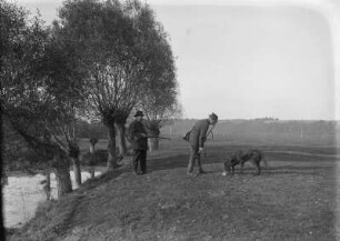 Zwei Jäger mit Hund auf einem Feld