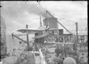 Passagiere an Deck des Hochseepassagierdampfers "Bremen" beobachten Arbeiten am Postflugzeugs HE 12 D-1717, welches noch auf der Katapultbahn befestigt ist