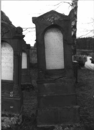 Grabstein 165 (Index: 100114998) Material: Sandstein und ? Zustand: beschädigt, Text sehr gut Maße HxBxT: 230x68x32 cm Beschreibung: Stele auf gestuftem Sockel, Spitzgiebel mit Eckakroteren, Texttafel mit Rundbogen: Grabstein 165