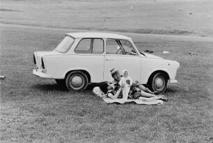 Junge Familie mit PKW "Trabant" auf einer Wiese