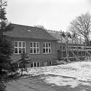 Volkshochschule Barsbüttel-Stellau: Erweiterungsbau: Richtfest: hinten rechts Gebäudeteil mit Gerüsten: im Dachgeschoss zwischen Dachsparren Arbeiter beim Anbringen der Richtkrone: links altes Gebäude: Winter