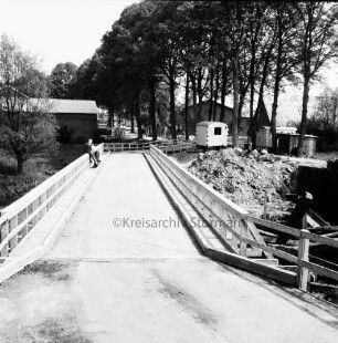 Heilsau: Brückenbau: gesperrte Landesstraße zwischen Zarpen und Reinfeld: provisorische Holzbrücke: hinten Bauwagen: dahinter Bauernhäuser und Bäume