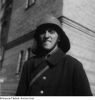 Berlin (West). Brandbekämpfung in einem Lagergebäude. Feuerwehrmann in Einsatzuniform. Feuerwehrschutzhelm und Nackenleder