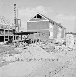 Lottbek: Volksschule Hoisbüttel: Teichweg: Erweiterungsbau: Neubau vor Fertigstellung: hinten links Hausmeisterwohnhaus im Rohbau mit Gerüst: davor Lastenaufzug, Holzschuppen, Bretterstapel und Sandhaufen: rechts Stapel mit Ziegeln