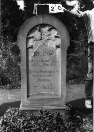 Grabstein 20 (Index: 99792912) Material: Sandstein Zustand: sehr stark verwittert im oberen Teil Maße HxBxT: 134x58x33 cm Beschreibung: Stele, Sockel profiliert, Rundbogenabschluß, Schriftfeld eingetieft in gleicher Form, Rundbogenfries Besonderheit: Schrift vergoldet: Grabstein 20