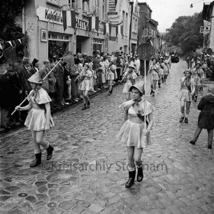 Karpfenfest: Umzug: Matthias-Claudius-Straße / Ahrensböker Straße (hinten): Fischerinnengarde mit Keschern: an den Straßenrändern Zuschauer: links Haus mit Ladenschild "Kolonialwaren", Fahnenschmuck, Wimpelgirlande: hinten rechts Hausecke von "Hotel Stadt Hamburg", 8. Oktober 1961