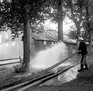 Gut Altfresenburg: Brand des Bullenstall: vorne ein geplatzter Wasserschlauch, rechts ein Feuerwehrmann, dahinter das brennende Gebäude