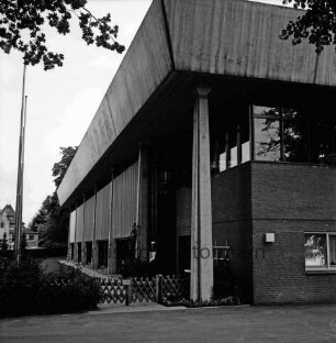 Stormarnhalle: Am Bürgerpark: vorn links Zaun, Büsche und Fahnenmasten: hinten Wohnhaus