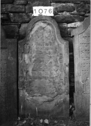 Grabstein 1076 (Index: 99630579) Material: Sandstein Zustand: völlig abgeblättert Maße HxBxT: 118x56x8 cm Beschreibung: Stele mit eingezogenem Rundbogenabschluß, Schriftfeld eingetieft: Grabstein 1076