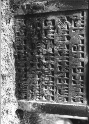 Grabstein 18 (Index: 100110924) Material: Sandstein Zustand: im Giebel Abschieferungen mit großem Textverlust, im unteren Teil leicht verwittert mit geringem Textverlust, eingesunken Maße HxBxT: 95x73x11 cm Beschreibung: Stele, Rundbogenabschluß mit Rundbogenfries, Schriffelder eingetieft Symbolik: 3 Rosetten: Grabstein 18B
