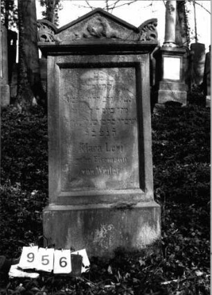 Grabstein 956 (Index: 99802652) Material: Sandstein Zustand: verwittert/Textverlust Maße HxBxT: 136x61x27 cm Beschreibung: Sockel, Stele mit verdachtem Giebel, Seitenakroterien Symbolik: Kranzgebinde, Akroterien mit Akanthusblättern: Grabstein 956