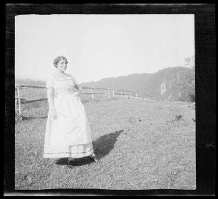 Gegend von Schliersee (Lkr. Miesbach): Frau in einem hellen Dirndl auf einer Bergwiese vor einem Gatter