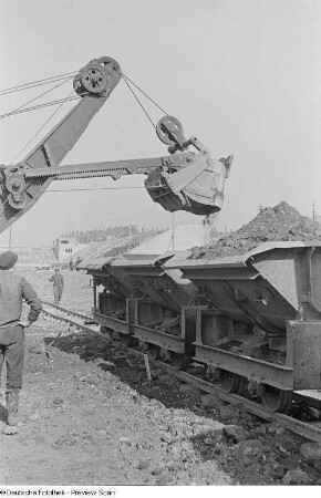 Verladen von Steinen und Erde mit Hilfe eines Baggers auf eine Trümmerbahn