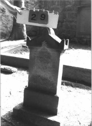 Grabstein 29 (Index: 100105726) Material: Sandstein Zustand: vollständig verwittert Maße HxBxT: 77x34x14 cm Beschreibung: Stele, getreppter Sockel, Giebel mit Akroteren: Grabstein 29