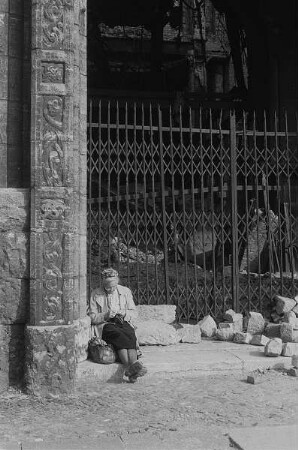 Berlin. Alte Frau sitzt auf einem Stein am Eingang einer Ruine und strickt