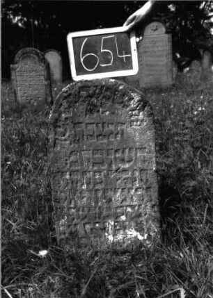 Grabstein 654 (Index: 100104937) Material: Sandstein Zustand: unten stark verwittert, eingesunken, teilweiser Textverlust Maße HxBxT: 71x42x10 cm Beschreibung: Stele, unregelmäßiger Rundbogenabschluss: Grabstein 654