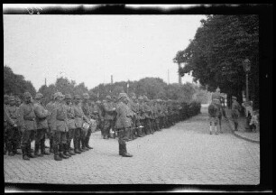 Nicht identifizierbare Ortschaft in Nordfrankreich oder Belgien: Soldaten mit Pickelhaube in Aufstellung auf einer breiten gepflasterten Parkstraße, davor ein Offizier zu Pferd (Seitansicht)