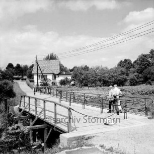 Heilsau (Abschnitt Mühlenau): Brücke in Fortsetzung der Eichbergstraße: Geländer, Kette, Verkehrsschild Durchfahrt gesperrt: Fußgänger auf Brücke: hinten Wanderweg: Wohnhaus, Obstgärten