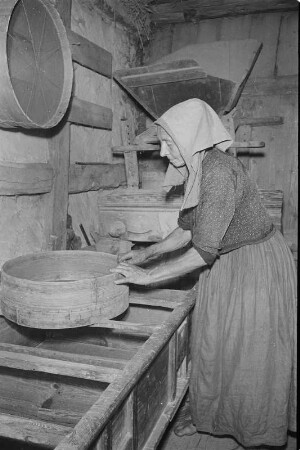 In der Graupenmühle in Tätschwitz. Frau in Hoyerswerdaer Arbeitstracht bei der Verarbeitung von Graupen. : Holanska kruparka při dźěle w Ptačecach.
