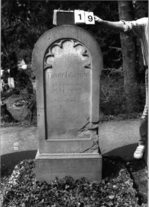 Grabstein 19 (Index: 99792910) Material: Sandstein Zustand: beschädigt Maße HxBxT: 140x56x30 cm Beschreibung: Stele, Sockel profiliert, Rundbogenabschluß, Schriftfeld eingetieft in gleicher Form, Rundbogenfries: Grabstein 19